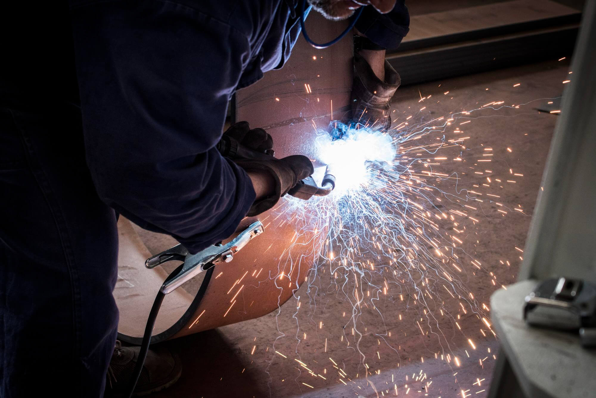 Hitsaaja työssään metalliputken hitsaamisessa, josta roiskuu kipinöitä.
